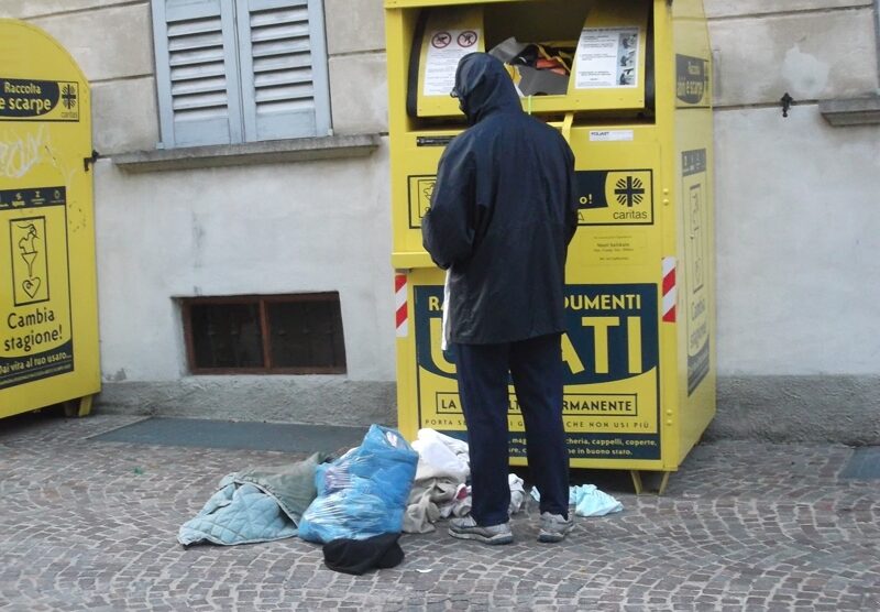 Un povero cerca degli indumenti in un container della Caritas