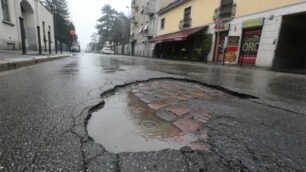 Una buca nell’asfalto in via Lecco. Sotto s’intravede la vecchia pavimentazione in porfido