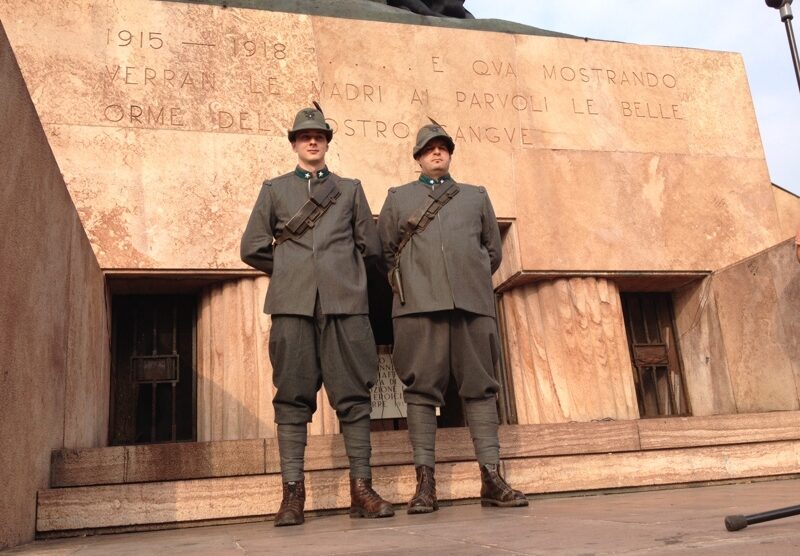 Due alpini in uniforme d’epoca davanti al monumento ai Caduti