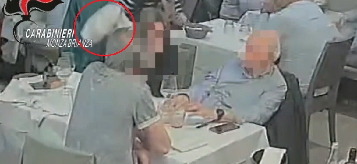 Nel cerchio rosso, la ladra che, con un tovagliolo in mano, sfila il portafoglio dalla borsetta di una cliente al tavolo di un locale